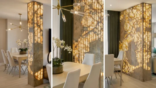 A luxurious dining room, reminiscent of a UK Property Award winner, features a tabletop with a modern chandelier above, surrounded by white chairs. A striking Patagonian stone column with backlit patterns stands nearby, enhancing the elegant ambiance of the space.