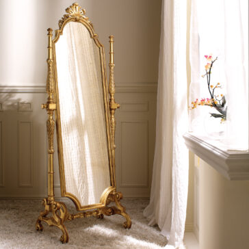 Freestanding Rococo Style Tilting Mirror A vintage Freestanding Rococo Style Tilting Mirror with ornate gold carvings stands elegantly on a plush white carpet. Sunlight filters through a window draped with sheer curtains, creating gentle shadows. A vase filled with delicate flowers adorns the windowsill.