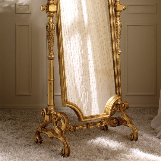 Freestanding Rococo Style Tilting Mirror A Freestanding Rococo Style Tilting Mirror with a vintage gold frame rests elegantly on a plush, light-colored carpet. This exquisite mirror reflects patterned curtains, creating a classic and elegant ambiance in the room.