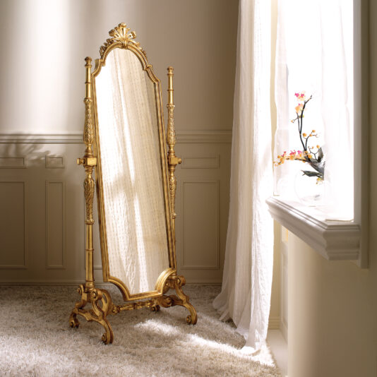 Freestanding Rococo Style Tilting Mirror A tall Freestanding Rococo Style Tilting Mirror graces a plush beige carpet in a softly lit room. Sunlight filters through sheer curtains, casting light on the mirror and an orchid in a vase on the windowsill. The elegantly paneled walls add to the room's sophistication.