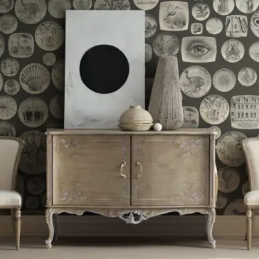 High End Rococo Inspired Cabinet A luxurious cabinet, drawing inspiration from Rococo design with intricate carvings, is positioned against a wall decorated with round, vintage prints. Atop this High End Rococo Inspired Cabinet are a substantial abstract canvas, a textured vase, and a ceramic pot. Two elegant chairs tastefully complement this stunning piece of furniture.
