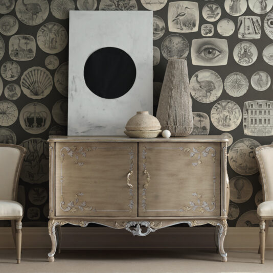 A luxurious cabinet, drawing inspiration from Rococo design with intricate carvings, is positioned against a wall decorated with round, vintage prints. Atop this High End Rococo Inspired Cabinet are a substantial abstract canvas, a textured vase, and a ceramic pot. Two elegant chairs tastefully complement this stunning piece of furniture.