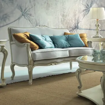 A vintage-inspired living room highlights a luxurious High End Rococo Style Sofa embellished with gold and teal pillows, accompanied by an ornate side table featuring a lamp. A matching coffee table displays elegant decor, while the textured wall with its subtle botanical design harmonizes beautifully with the beige carpet.