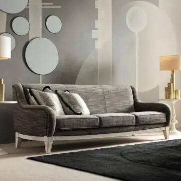 Large Art Deco Style Sofa A contemporary living room showcasing the Large Art Deco Style Sofa in sleek gray, enhanced by two decorative pillows and accompanied by sophisticated table lamps. The backdrop highlights geometric wall art featuring circles and abstract shapes, beautifully complementing the dark area rug on the floor.