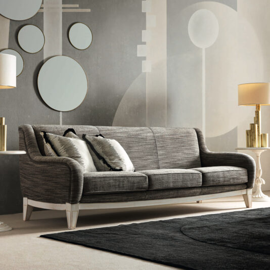 A contemporary living room showcasing the Large Art Deco Style Sofa in sleek gray, enhanced by two decorative pillows and accompanied by sophisticated table lamps. The backdrop highlights geometric wall art featuring circles and abstract shapes, beautifully complementing the dark area rug on the floor.