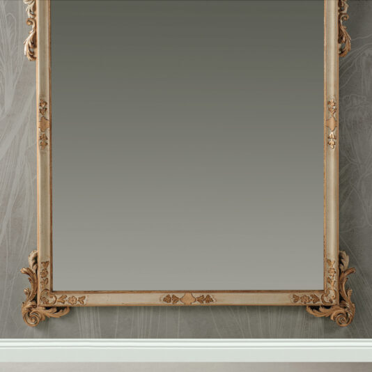 Large Baroque Style Wall Mirror The Large Baroque Style Wall Mirror, featuring an intricately carved wooden frame, is mounted on a wall adorned with patterned wallpaper; its ornate design captures the timeless elegance of bygone eras. The mirror reflects the texture of the wall along with a portion of the floor beneath.