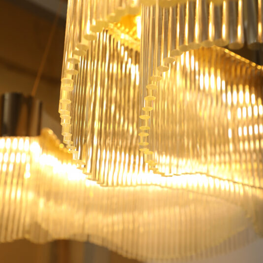 Large Modern Wavy Chandelier A close-up of the Large Modern Wavy Chandelier showcases its cascading glass elements. Warm light bathes the fixture, creating a glowing and elegant ambiance while highlighting its textured design as a stunning centerpiece.