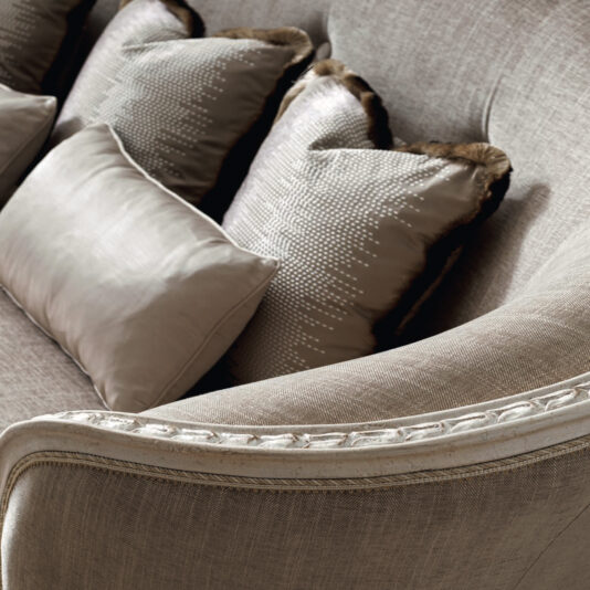 Large Rococo Style Curved Sofa Here's a rewrite of the sentence based on the provided product data:
A close-up of the Large Rococo Style Curved Sofa showcases its stylish design, featuring a textured beige upholstery complemented by decorative pillows with a mix of silky and patterned finishes. The elegant piece is characterized by gently curved armrests and detailed piping.