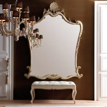 Large Rococo Style Wall Mirror The elegant room features a Large Rococo Style Wall Mirror with a decorative frame. Below the mirror is a cushioned bench with elegantly curved legs. On the left, a classic chandelier adorned with black lampshades hangs, offering a striking contrast to the brown and white walls.