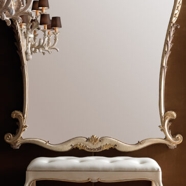 Large Rococo Style Wall Mirror A Large Rococo Style Wall Mirror with an intricately carved frame is mounted on a brown wall. A white cushioned bench sits below it. To the left, a decorative wall sconce with black lampshades adds elegance to the scene.