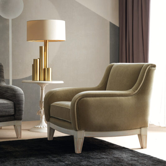 The stylish living room is adorned with a Modern Deco Armchair in olive-green, positioned beside a round white side table topped with a gold lamp. Geometric wall patterns and an extensive dark curtain enhance the background, while a plush dark rug ties together the elegant ambiance.