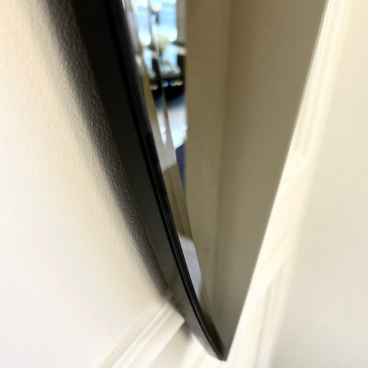 A close-up side view features a flat-screen TV and the Modern Pointed Oval Bronze Wall Mirror. Both are mounted on a white wall, showcasing the slim profile and glossy finish of the TV, while the elegant mirror enhances the overall sleek design with its stylish presence.