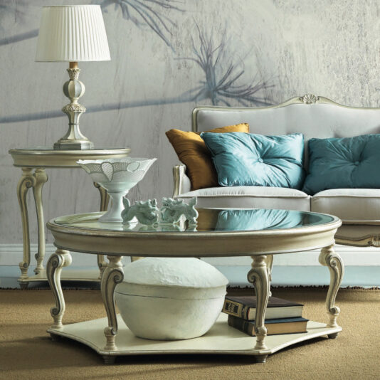 A refined living room showcases a Rococo Style Rectangular Glass Coffee Table, complemented by an elaborate lamp on a side table and a luxurious sofa adorned with teal and mustard cushions. The space exudes sophisticated, classic decor with a neutral palette and features a textured wall in the background.