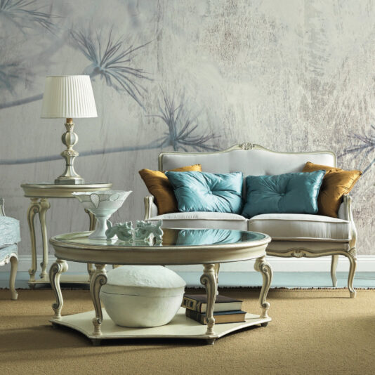 Rococo Style Round Glass Coffee Table In a vintage-inspired living room, a white sofa is complemented by blue and gold cushions, while the Rococo Style Rectangular Glass Coffee Table showcases decorative items and books. The space is further enhanced with an elegant side table holding a lamp and walls featuring abstract floral patterns on a soft background.