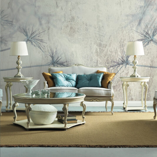 Rococo Style Round Glass Side Table A classic living room showcases a vintage white sofa decorated with blue and gold cushions, framed by ornate coffee tables. Rococo Style Round Glass Side Tables add an elegant touch, while two matching lamps brighten the beige rug on the floor, enhancing the subtle floral pattern of the wallpaper.