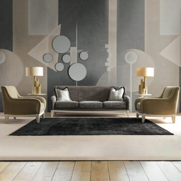 Rococo Style Round Side Table A modern living room with a gray geometric mural features a gray sofa, two olive armchairs, and two gold lamps with white shades. A Rococo Style Round Glass Side Table adds elegance, while a black rug rests on the beige floor. Circular wall accents enhance the decor.
