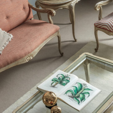 Small Rococo Style Day Sofa A sophisticated living room is highlighted by a vintage Small Rococo Style Day Sofa, paired with a side table and a glass coffee table. The coffee table holds an open book displaying botanical illustrations next to decorative golden orbs. The decor incorporates a soft color palette and timeless designs.
