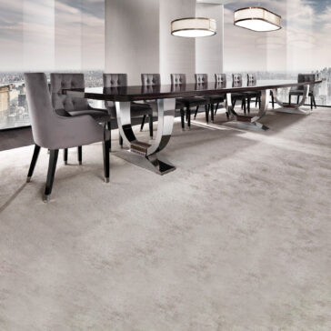 A modern conference room showcases a commanding Large 6 Metre Italian Dining Table surrounded by upholstered chairs. Two circular pendant lights hang from the ceiling, while large windows provide cityscape views, and a light-colored carpet enhances the room's elegance.