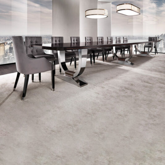 A modern conference room showcases a commanding Large 6 Metre Italian Dining Table surrounded by upholstered chairs. Two circular pendant lights hang from the ceiling, while large windows provide cityscape views, and a light-colored carpet enhances the room's elegance.