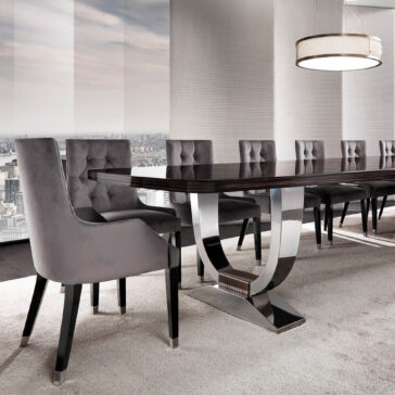 In a contemporary dining room, a Large 6 Metre Italian Dining Table takes center stage, featuring sleek metallic legs and a dark glossy surface. Surrounding this impressive table are eight gray cushioned chairs. Expansive windows provide a panoramic city view, complemented by the round pendant light hanging above.