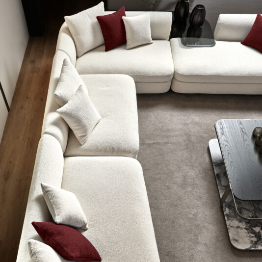Large Modular Contemporary Corner Sofa A modern living room showcases the Large Modular Contemporary Corner Sofa, embellished with red and white pillows. This contemporary sofa sits on a light brown carpet beside a sleek black coffee table, enhanced with matching decorative accents.