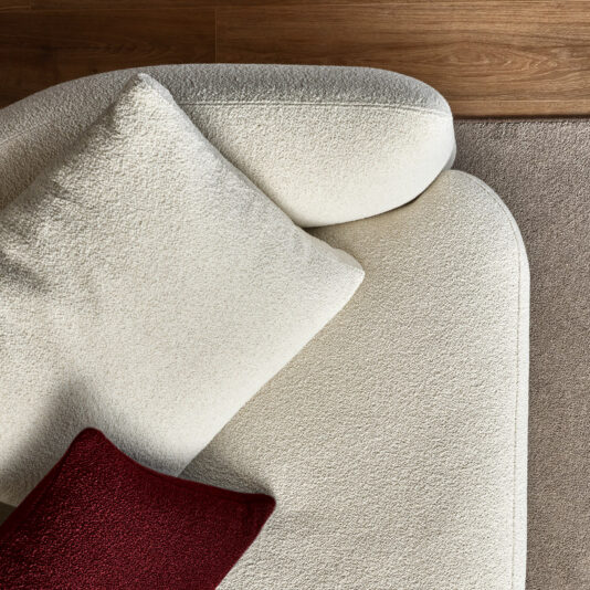 Large Modular Contemporary Corner Sofa From above, you can see the Large Modular Contemporary Corner Sofa in beige, paired with a matching pillow and a contrasting dark red one. It sits atop a tan carpet, framed by light wood flooring, all contributing to a warm and cozy ambiance.