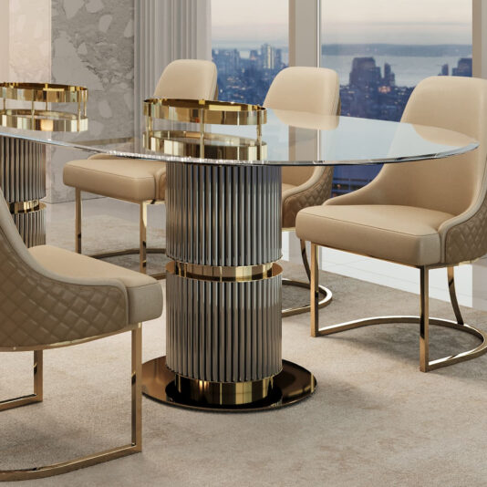 A contemporary dining room features the Contemporary Oval Glass Dining Set with a glass-topped table, decorative gold and silver cylindrical base, and beige upholstered chairs with gold accents. Tall windows reveal a cityscape and waterfront view in the background.
