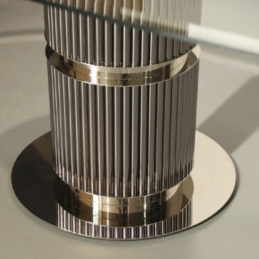 Close-up of a sleek, metallic ribbed cylindrical structure on a round base resembling the Contemporary Oval Glass Dining Table, with its reflective surface capturing light and a glass piece visible at the top edge.