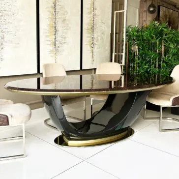 Exclusive Oval Designer Dining Table A modern dining room showcases the Exclusive Oval Designer Dining Table with a sculptural black and gold base, cream upholstered chairs, abstract wall art behind it, and a tall indoor plant for added elegance.