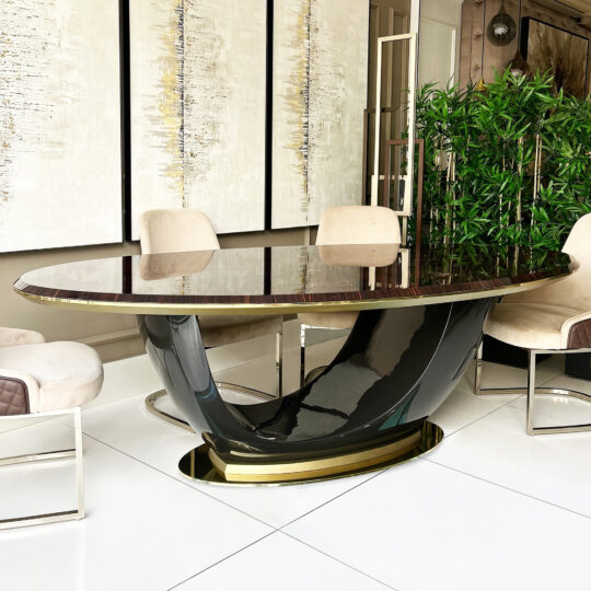 A modern dining room showcases the Exclusive Oval Designer Dining Table with a sculptural black and gold base, cream upholstered chairs, abstract wall art behind it, and a tall indoor plant for added elegance.