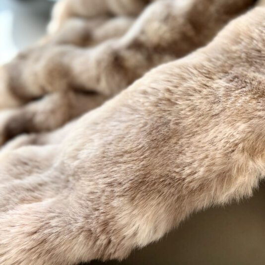Close-up of the Beige Textured Faux Fur Throw reveals its plush, smooth surface. The mix of light and dark shades adds depth, mimicking the softness and inviting warmth of fine fur.