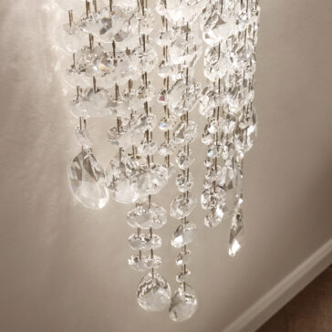 Contemporary Cut Crystal Wall Light A close-up of the Contemporary Cut Crystal Wall Light showcases faceted glass pieces reflecting light. The varying shapes of the crystals, attached to metal fixtures, set against a light wall background, create a stunning interplay of light and elegance.