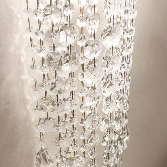 Close-up of a Contemporary Cut Crystal Wall Light featuring multiple rows of sparkling cut crystal beads, softly lit against a white background. The crystals cast gentle reflections and refractions, reminiscent of chandelier light patterns.