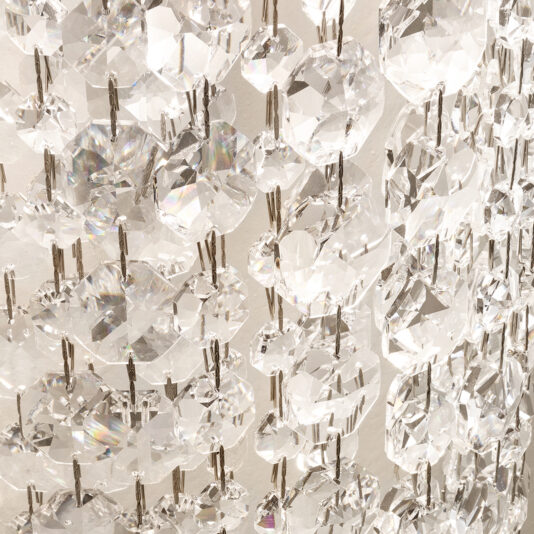 Contemporary Rectangular Cut Crystal Chandelier The Contemporary Rectangular Cut Crystal Chandelier features a close-up view with rows of sparkling crystal prisms against a white backdrop, where light dances through to create dazzling effects, small rainbows, and intricate patterns.
