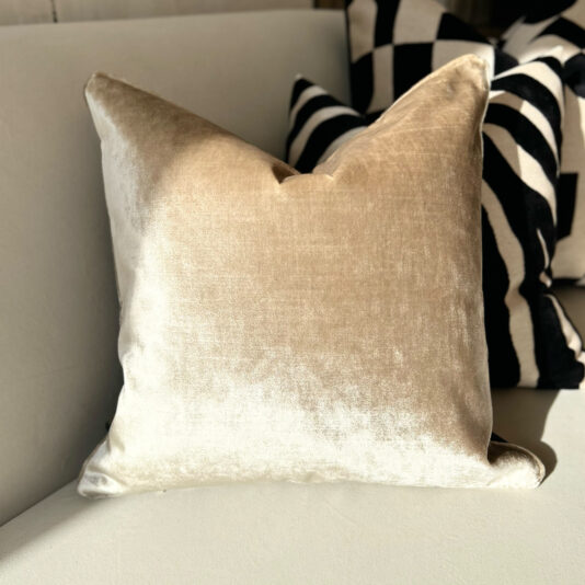 A Luxury Velvet Double Sided Scatter Cushion in beige adorns a light-colored couch, complemented by a black and white scatter cushion featuring bold, wavy stripes.