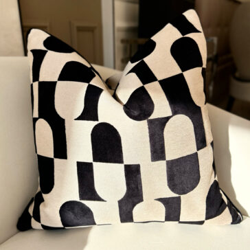 Luxury Velvet Retro Pattern Scatter Cushion The Luxury Velvet Retro Pattern Scatter Cushion, featuring a bold black and white geometric design with capsule-like abstract shapes, is displayed on a light-colored chair. Sunlit soft shadows on the plush fabric enhance its elegant charm.