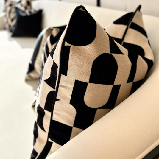 A close-up of a modern sofa features Luxury Velvet Retro Pattern Scatter Cushions, displaying a bold black abstract design on beige. These cushions are neatly placed against the soft white upholstery, crafting a stylish and cozy ambiance.