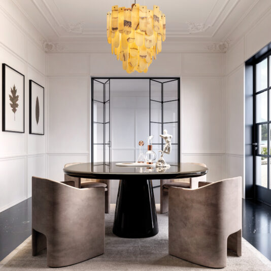 A modern dining room showcases a sleek black onyx oval table with four beige chairs on a gray rug. A distinctive yellow Modern Onyx Oval Chandelier hangs overhead, casting a warm glow. Black-framed leaf art decorates the walls, complemented by large windows for an open and airy feel.