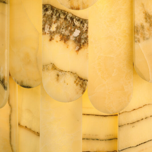 The image showcases a close-up of layered yellow marble or onyx with brown veining and textured patterns, reminiscent of the Modern Onyx Tiered Ceiling Light. It highlights the smooth, semi-translucent surface and wavy edges, creating an abstract and intricate design.