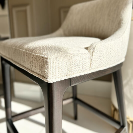 Set Of Two Boucle Bar Stools A beige upholstered chair with textured fabric and dark wooden legs enhances a well-lit room, pairing perfectly with the