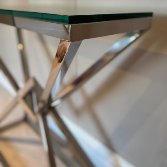 Contemporary Stainless Steel Glass Console Table The Contemporary Stainless Steel Glass Console Table boasts a green glass top with metallic angular legs, emphasizing geometric design. Its gold accents are highlighted by a softly blurred background, enhancing the table's modern allure.
