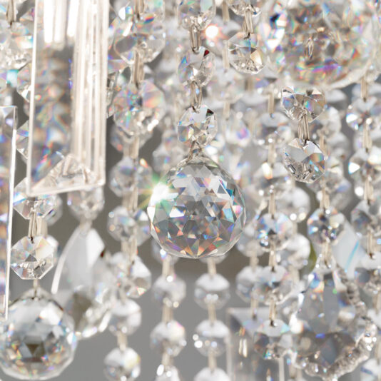 A close-up of the Oval Cut Crystal Pendant Chandelier reveals its sparkling beauty. Various sizes of faceted crystal beads reflect and refract light, casting rainbow patterns. The intricate arrangements hang elegantly, showcasing their brilliance.