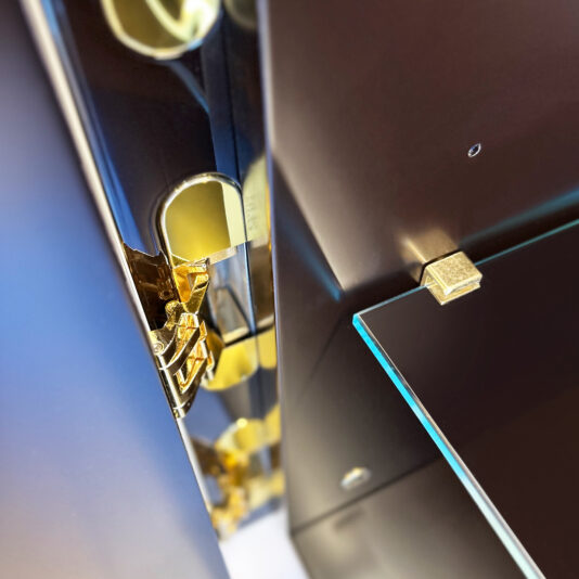 Close-up of a glass shelf with a gold bracket inside a dark cabinet, featuring gold hinges and reflections that highlight the luxurious, modern design of the Luxury Art Deco Style Sunburst Sideboard.