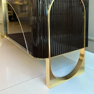 Luxury Art Deco Style Sunburst Sideboard A close-up of the Luxury Art Deco Style Sunburst Sideboard, featuring glossy dark ribbed panels and gold metal legs in a geometric semi-circular design, displayed on a white tiled floor.