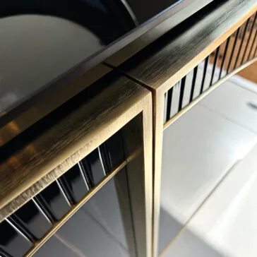 Luxury Art Deco Style Sunburst Sideboard Close-up of the Luxury Art Deco Style Sunburst Sideboard corner, showcasing its brushed gold metallic edges and glossy black panels that reflect light, highlighting its sleek and modern Art Deco-inspired design.