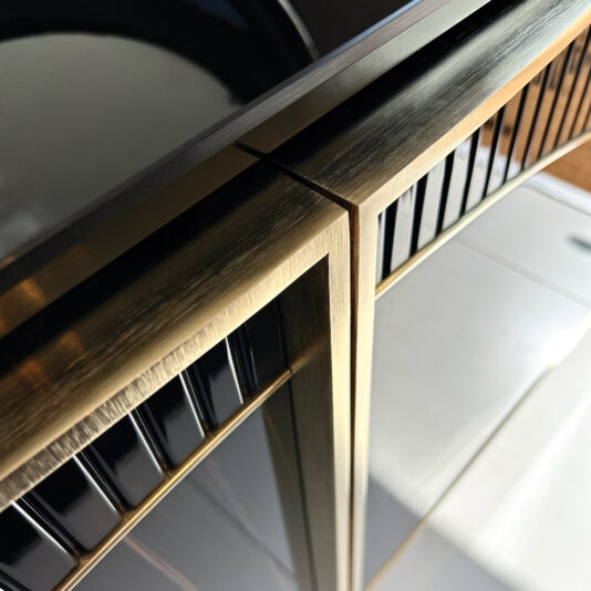 Close-up of the Luxury Art Deco Style Sunburst Sideboard corner, showcasing its brushed gold metallic edges and glossy black panels that reflect light, highlighting its sleek and modern Art Deco-inspired design.