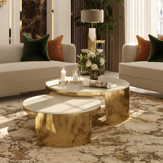 A luxurious living room features two Modern Marble Set Of Coffee Tables on a patterned rug, surrounded by cream sofas with dark green and burnt orange cushions. The tables are adorned with a vase of flowers and candles, while warm lighting highlights the elegant decor.