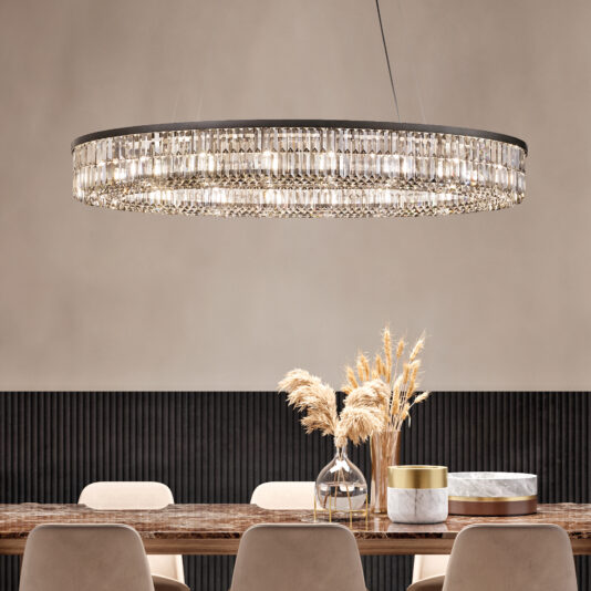 A dining room features a Narrow Smoked Cut Crystal Chandelier above a wooden table decorated with vases of dried pampas grass and two decorative boxes, surrounded by four beige chairs against a textured wall.