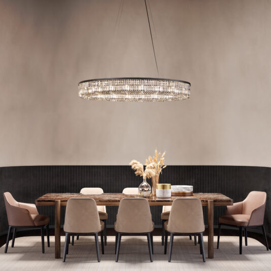 A dining room showcases a wooden table set for eight, including beige chairs and a black cushioned bench. Overhead, the Narrow Smoked Cut Crystal Chandelier adds elegance. A decorative vase with pampas grass adorns the table against a muted wall background.