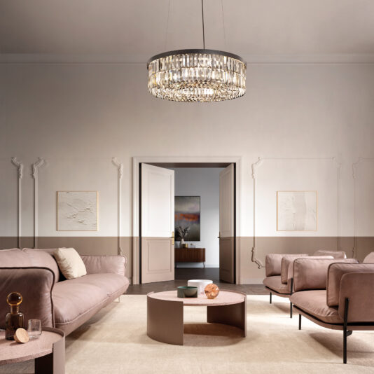 Modern Smoked Cut Crystal Chandelier A modern living room with beige walls and elegant molding features a magnificent Modern Onyx Chandelier. It includes two plush sofas, a round coffee table, and minimalist artwork on the walls. A partially open door hints at a painting in the adjoining room.